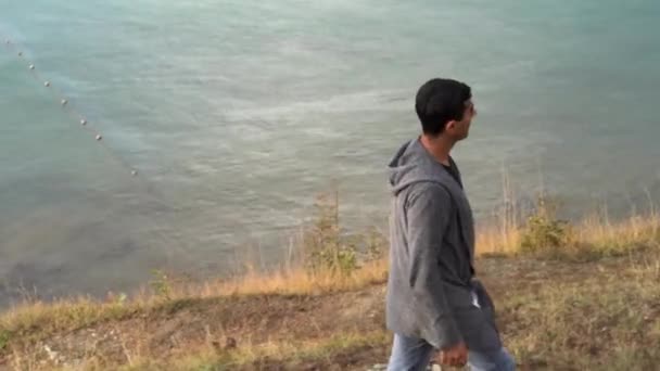 Mężczyzna spacerujący samotnie na wybrzeżu Morza Czarnego jesienią. Media. Młoda kobieta z czarnymi włosami spacerująca po żółtej trawie wzgórza wzdłuż morza i myśląca o czymś. — Wideo stockowe