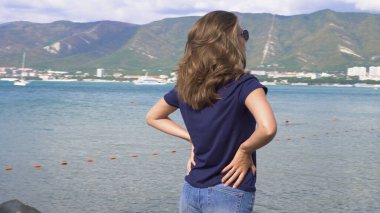 Sahildeki kadın ve dağlı deniz manzarası. Medya. Güzel, genç bir kadın tatilde, deniz ve dağ manzaralı yoğun plajda dinleniyor.