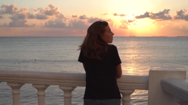 Attraktiv kvinna står vid räcke på bakgrunden av solnedgången. Media. Vacker kvinna njuter av kvällen stående på banvallen med utsikt över havet horisont. Vacker solnedgång med havsutsikt — Stockvideo