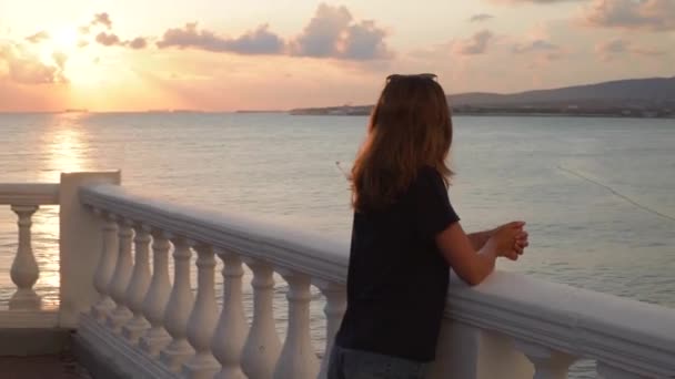 Kvinna på vall vid solnedgången. Media. Ung kvinna står vid räcke på bakgrunden havsutsikt vid solnedgången efter regn. Vackert landskap öppnar upp för attraktiv kvinna på banvallen — Stockvideo