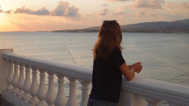 Gün batımında sette bir kadın. Medya. Yağmurdan sonra gün batımında arka plandaki korkuluklarda genç bir kadın duruyor. Güzel manzara setin üzerinde çekici bir kadına açılır.