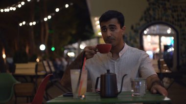 Adam kafedeki bardağa kaynar su döküyor. Medya. Çekici bir adam, kafenin yanındaki masada gece lambasıyla kahve içer. Adam açık kafede sevgilisini bekliyor.