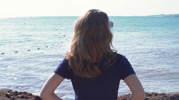 Mulher andando na praia no fundo do horizonte do mar. Mídia. Visão traseira da jovem mulher em shorts caminhando ao longo do caminho de madeira para o mar no dia ensolarado. Maravilhosas férias no mar — Fotografia de Stock