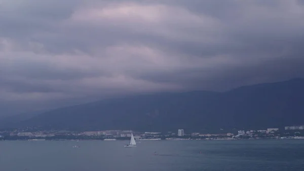 Vacker havsutsikt med stad på bergskusten i molnigt väder. Media. Naturskön utsikt över segelbåt på bakgrund av bergskusten med stad i molnigt väder — Stockfoto