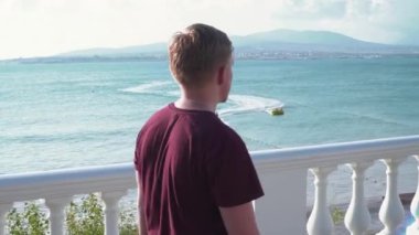 Genç adam güneşli bir günde denizin arka planında yürür. Medya. Genç adam güneşli bir günde güzel deniz kıyısında yürür. Adam deniz manzarasının arka planında yürüyor dağlarla ve kasabayla