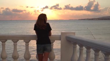 Gün batımında deniz manzaralı arka planda duran genç bir kadın. Medya. Çekici bir kadın arka planda, yağmurdan sonra güzel bir gün batımının üzerinde duruyor.