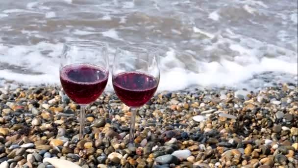 Dwa kieliszki wina z czerwonym winem na kamienistej plaży. Koncepcja. Koncepcja Walentynki, dwa przezroczyste kieliszki wina na żwirowej plaży nad morzem w słoneczny letni dzień. — Wideo stockowe