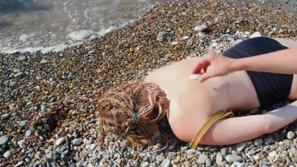 Kameny na zádech mladé ženy ležící na pláži. Koncept. Žena leží obličejem dolů na skále a kameny jsou umístěny na zádech. Žena odpočívá na pláži s kameny na zádech — Stock video