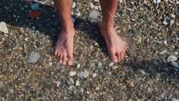 Mans Beine am felsigen Strand. Konzept. Großaufnahme eines Mannes, der auf einer Bank steht und Füße nass macht. Füße stehen auf Kieselsteinen mit ankommenden Wellen — Stockvideo