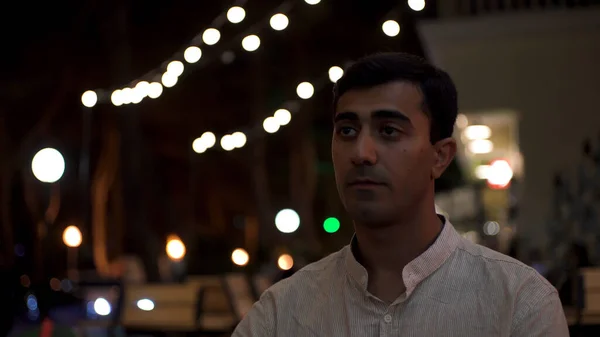 Triste hombre romántico soltero esperando a su novia en el restaurante al aire libre. Medios. Retrato de un hombre aburrido con camisa blanca sentado solo hasta tarde en la noche. — Foto de Stock