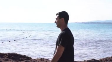 Kumsalda yalnız yürüyen yakışıklı genç adam. Medya. Güneşli bir yaz gününde, deniz kıyısında yavaşça yürüyen siyah saçlı bir erkek..