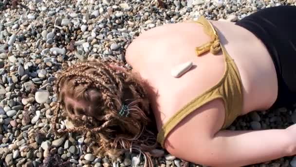 Genç bir kadın çakıl taşı plajında yatıyor. Kavram. Erkek eli sıcak taşları mayo giymiş genç bir kızın sırtına takıyor.. — Stok video