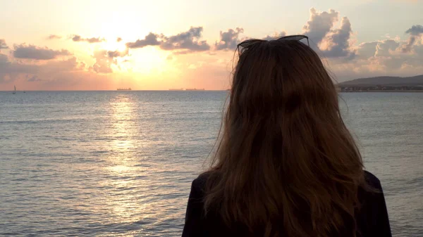 Młoda szczupła dziewczyna w czarnej koszuli stojąca nad morzem, opierająca się o poręcz podczas wschodu słońca. Media. Widok z tyłu szczupła kobieta korzystających zapierające dech w piersiach krajobraz morski. — Zdjęcie stockowe
