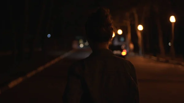 Fille en jeans bleu chemise courir dans la rue la nuit. Meida. Vue arrière d'une jeune femme courant dans la rue tard le soir le long des lampadaires. — Photo