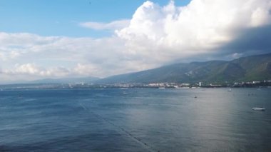 Kıyı kenti arka planında ve dağlarda küçük dalgalarla nefes kesici mavi okyanus manzarası. Kavram. Mavi bulutlu gökyüzü ile deniz manzarası, özgürlük ve tatil kavramı.