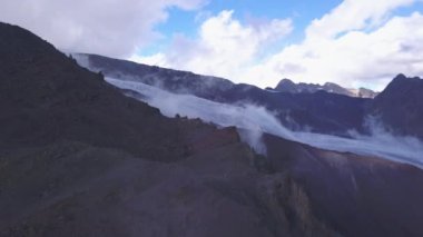 Soğuk zemin ve beyaz karla kaplı bir dağ yamacıyla inanılmaz bir manzara. Şarjör. Mavi bulutlu arka planda, tepeye doğru kayan bulutların hava görüntüsü..