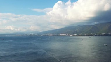 Kıyı kenti arka planında ve dağlarda küçük dalgalarla nefes kesici mavi okyanus manzarası. Kavram. Mavi bulutlu gökyüzü ile deniz manzarası, özgürlük ve tatil kavramı.