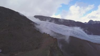 Soğuk zemin ve beyaz karla kaplı bir dağ yamacıyla inanılmaz bir manzara. Şarjör. Mavi bulutlu arka planda, tepeye doğru kayan bulutların hava görüntüsü..