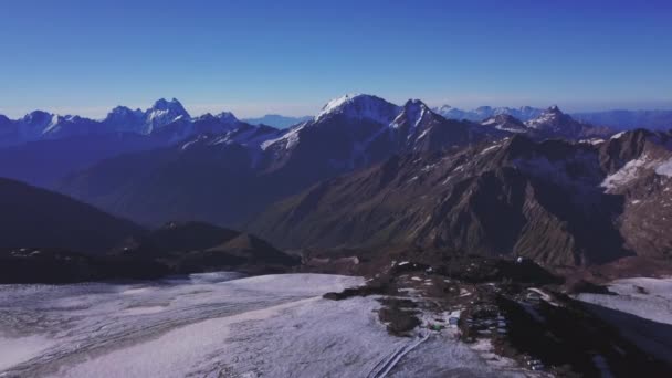 Вид з повітря на захоплюючий високий діапазон гір на фоні блакитного неба. Кліп. Політ над гігантськими пагорбами зі сніговими вершинами в сонячний день . — стокове відео