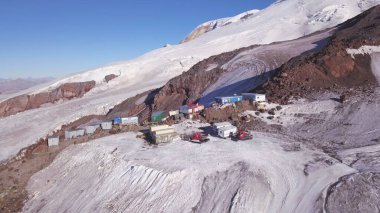 Kar, kış mevsiminde dağların zirvelerini tırmananlar için bir sığınak haline getirdi. Şarjör. Mavi gökyüzü arka planındaki gezginler ve dağcılar için karlı yamaçların ve çeşitli binaların havadan görüntüsü.