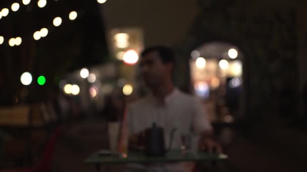 Portrait of a lonely man wearing white shirt sitting at the restaurant table. Media. Blurred effect of the male portrait with drinks on the table at outdoors terrace. — Stock Video