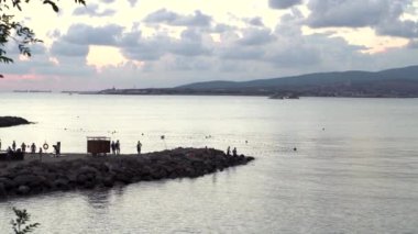 Yelkenli gemiler ve teknelerle Karadeniz 'in yukarısında gün batımı. Medya. Durgun suların kıyısında yürüyen insanlarla sonsuz bir ufuk çizgisi..