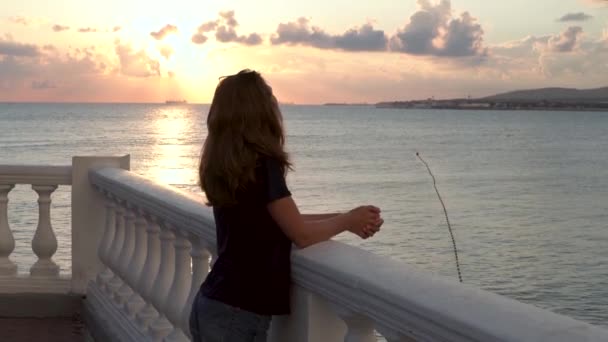 Vrouw die op de dijk aan de kust van de zee staat en kijkt naar een prachtige zonsondergang. De media. Eenzaam jong romantisch meisje leunend op de balustrade.. — Stockvideo
