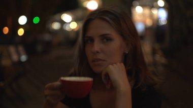 Şehirdeki güzel kadın portresi. Açık hava restoranının bulanık arka planında ve parlayan ışıklarda. Medya. Hassas seksi kız kameraya dışarı bakıyor..