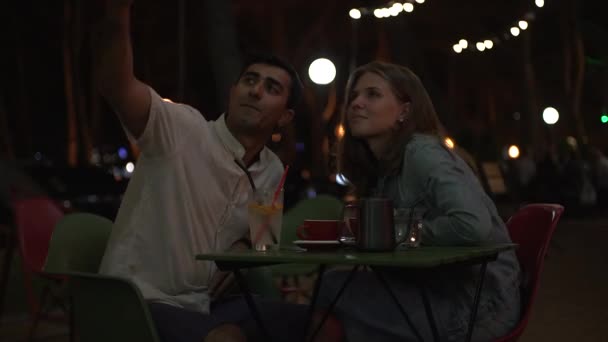 Casal jovem no jantar romântico tirando foto de retrato selfie com telefone inteligente. Mídia. Homem e mulher felizes passam o tempo juntos no terraço ao ar livre de um restaurante à noite no verão. — Vídeo de Stock