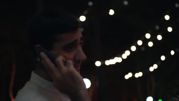 Портрет самотнього чоловіка в білій сорочці, що розмовляє на мобільному телефоні. Медіа. Розмитий ефект чоловічого портрета, використовуючи свій смартфон на вулиці вночі . — стокове відео