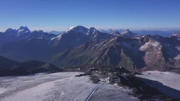 Vista aérea de tirar o fôlego de alta gama de montanhas no fundo do céu azul. Clipe. Voando sobre as colinas gigantes com picos nevados em um dia ensolarado. — Vídeo de Stock