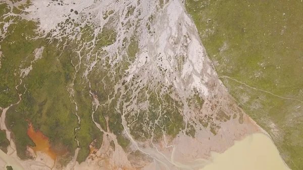 Terreno en montañas donde fluye el agua derretida. Clip. Vista superior de líneas sorprendentes en la superficie de las montañas de agua de fusión que fluye de los glaciares. Muddy ríos de montaña fluyen en el lago — Foto de Stock