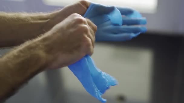 Közelről, ahogy férfi kezek kék védőkesztyűt húznak. A média. A hím orvosi kesztyűt visel a koronavírus elleni védelemhez COVID-19, az egészség fogalma. — Stock videók
