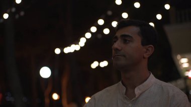 Genç yakışıklı adam şehir kafesinde oturuyor ve büyük kırmızı bir bardaktan sıcak içecek içiyor. Medya. Akşam kahve içen erkek siyah gökyüzü ve çelenk arka planında.