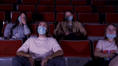 Sinemada film izleyen, tıbbi maske takan bir grup genç. Medya. Covid 19 salgını sırasında eğlence anlayışı, kadın ve erkek oturup film izliyor..
