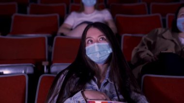 Karantinadaki sinema, koronavirüs salgını güvenlik kuralları, film izlerken sosyal mesafe. Medya. Güzel, uzun saçlı, koruyucu maskeli genç kadınlar oditoryum sıralarında oturuyorlar.