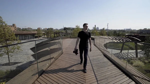 Homem caminhando sobre a construção incomum de Tyufeleva roshcha. Acção. Fotógrafo masculino em roupas pretas com uma câmera profissional andando em um parque moderno. — Fotografia de Stock