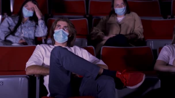 Sinemada film izleyen, tıbbi maske takan bir grup genç. Medya. Covid 19 salgını sırasında eğlence anlayışı, kadın ve erkek oturup film izliyor.. — Stok video