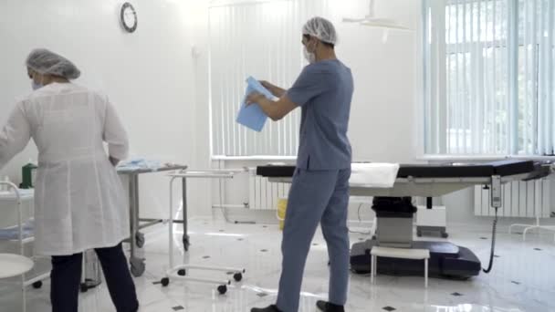 Enfermeras y enfermeras preparando una sala estéril para el procedimiento quirúrgico. Acción. Vista trasera de los cuidadores en una sala quirúrgica antes del procedimiento. — Vídeos de Stock