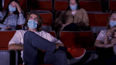 Sinemada film izleyen, tıbbi maske takan bir grup genç. Medya. Covid 19 salgını sırasında eğlence anlayışı, kadın ve erkek oturup film izliyor..