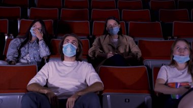 Sinemada film izleyen, tıbbi maske takan bir grup genç. Medya. Covid 19 salgını sırasında eğlence anlayışı, kadın ve erkek oturup film izliyor..