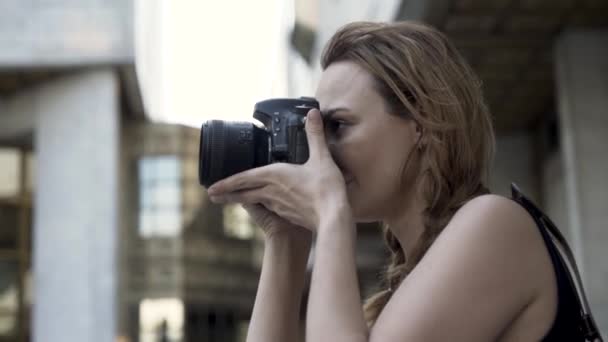 Fotografka s profesionální kamerou. Akce. Mladá žena drží fotoaparát v rukou a fotit na ulici procházka po skleněné fasádě budovy rozmazané pozadí. — Stock video