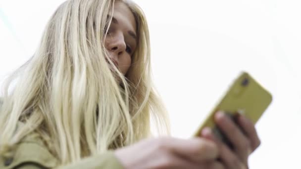 Vue du bas de la jeune femme attrayante en utilisant le téléphone à l'extérieur. Les médias. Femme avec des cheveux longs tapant le message texte sur le téléphone portable en été. — Video