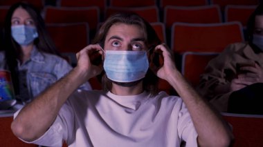Sinemadaki koruyucu maskeli insanlar fiziksel temastan kaçınmak için mesafeyi koruyorlar. Medya. Coronavirus COVID-19 hastalık koruması, bunu takan genç bir adama tıbbi maske takan kadın eli.