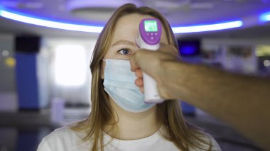 Koronavirüs COVID-19 'un taranması ve korunması için ateşini dijital termometreyle kontrol edin. Medya. Bir adamın alnında termometre ile vücut ısısını ölçmeye çalışması...