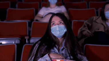 Karantinadaki sinema, koronavirüs salgını güvenlik kuralları, film izlerken sosyal mesafe. Medya. Güzel, uzun saçlı, koruyucu maskeli genç kadınlar oditoryum sıralarında oturuyorlar.