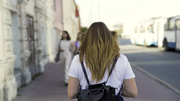 Vista trasera de una joven en una calle urbana en el verano. Medios. Mujer de camisa blanca con el pelo largo caminando sobre el fondo de la ciudad. — Foto de Stock
