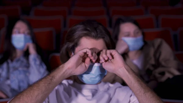 Lidé v modrých lékařských maskách v dobách epidemie koronaviru, sledující film v kině. Média. Portrét unaveného muže, který si mnul oči. — Stock fotografie
