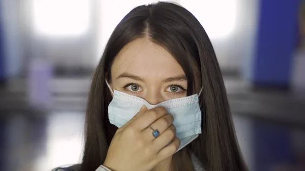 Mladá žena si nasazuje masku v divadelním sále. Média. Detailní záběr mladé brunetky dívka uvedení na lékařské masky na pozadí kinosálu. — Stock fotografie