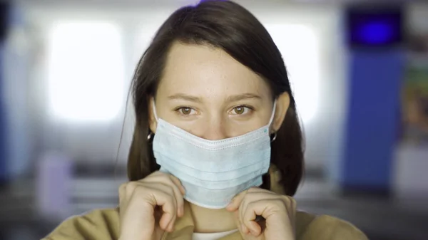 Young woman putting on face mask in movie theater hall. Media. Close up of brunette young girl putting on medical mask on the background of cinema hall.